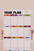 Person holding bold, colorful year overview calendar against pink background