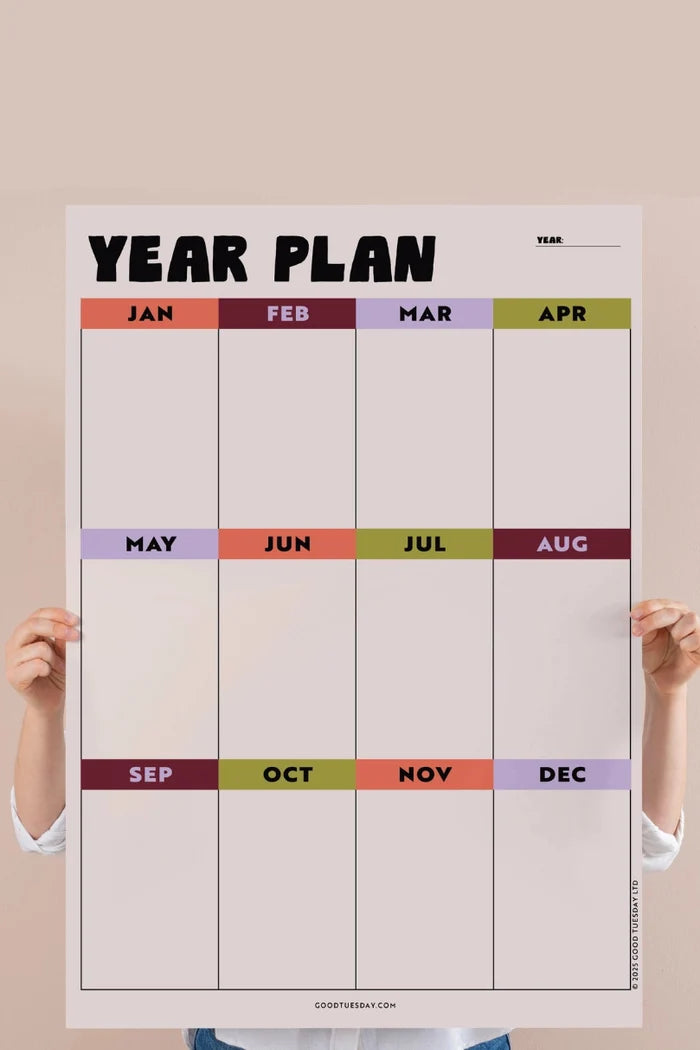 Person holding bold, colorful year overview calendar against pink background
